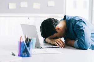 asiatisk affärsman somnar på sitt skrivbord från överansträngning foto