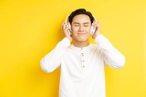 foto av asiatisk man i vit skjorta som lyssnar på musik med slutna ögon på gul bakgrund