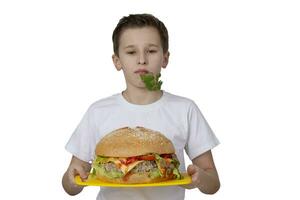 ung pojke med stor hamburgare isolerat i vit. en tonåring är innehav en burger och en knippa av persilja. foto