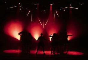 mörk silhuetter av dans flickor mot de bakgrund av röd ljus från skede strålkastare. foto