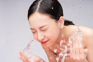 vacker asiatisk kvinna tvättar ansiktet med rent vatten foto