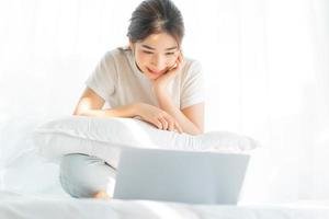 ung asiatisk kvinna som sitter på sängen och tittar på hemunderhållning