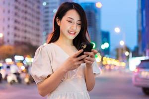 ung asiatisk kvinna som använder smarttelefonen på gatan på natten