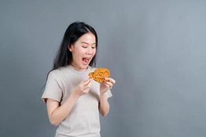 ung asiatisk kvinna som bär en tröja med ett lyckligt ansikte och tycker om att äta stekt kyckling på grå bakgrund foto
