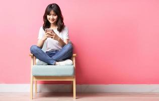 asiatisk kvinna som sitter på soffan med sin telefon med ett lyckligt uttryck
