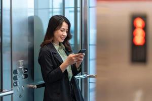 porträtt av ung affärskvinna som står i hiss och använder telefonen foto
