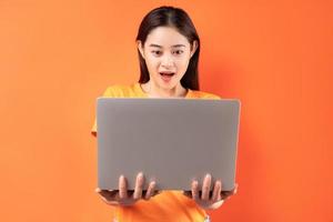 asiatisk kvinna som håller bärbara datorn i hand med ett förvånat uttryck