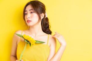 vacker asiatisk kvinna som håller och poserar med solros på gul bakgrund foto