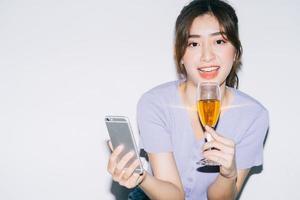 ung asiatisk kvinna som dricker vin och använder smartphonen på vit bakgrund
