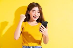 ung asiatisk tjej som använder smarttelefonen på gul bakgrund