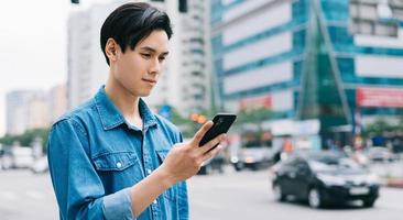 ung asiatisk man går och använder smartphone på gatan