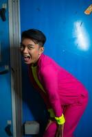en Gay asiatisk man Framställ mycket rolig och humoristisk medan bär en rosa kostym i främre av en blå bakgrund foto