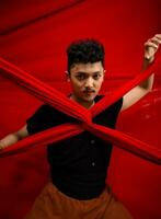 ett asiatisk man står i främre av en röd x-formad trasa och innehar den med både händer foto