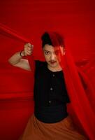 ett asiatisk man i en svart skjorta beläggning hans ansikte med en röd trasa med en skrämmande ansiktsbehandling uttryck i främre foto