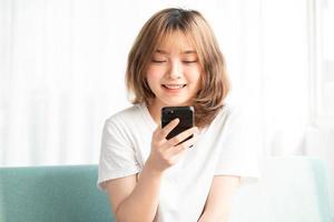 ung asiatisk tjej som sitter i soffan med telefonen med ett glatt ansikte