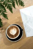 kaffe kopp och en del av bok på trä tabell med prydnad ormbunke blad foto