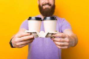 närbild foto av leende skäggig hipster man håller två papper kaffe koppar ta bort