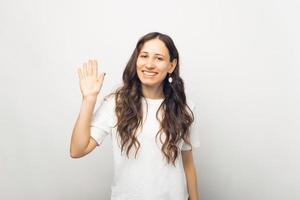 porträtt av glad ung kvinna i vit t-shirt gör hej gest