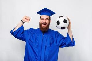 förvånad student man i ungkarl firar och håller fotboll foto