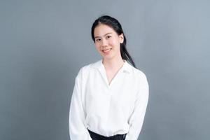 glad asiatisk kvinna med lyckligt ansikte i vit skjorta på grå bakgrund