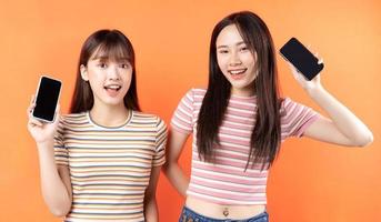 två vackra unga asiatiska flickor som använder mobiltelefoner på orange bakgrund foto