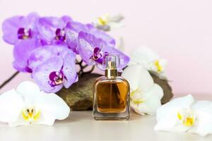 en parfym flaska står på en sten mot en bakgrund av skön orkidéer. eleganta utseende, layout, personlighet. baner, en plats för de text. foto