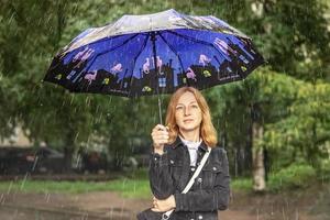 en ung kvinna står i regnet på gatan under ett paraply. regnig dag foto