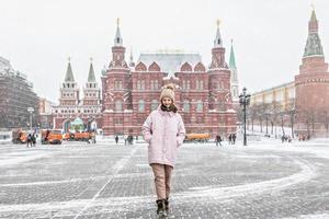 en vacker ung flicka i en rosa jacka går längs manezhnaya torget i Moskva under ett snöfall och snöstorm. snöslungor arbetar i bakgrunden.
