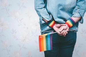asiatisk dam som bär blå jeanjacka eller jeansskjorta och håller regnbågens färgflagga, symbol för HBT stolthet månad firar årliga i juni sociala av homosexuella, lesbiska, bisexuella, transpersoner, mänskliga rättigheter.
