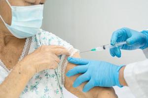 äldre asiatisk äldre kvinna som bär ansiktsmask får covid-19 eller coronavirusvaccin av läkare gör injektion. foto