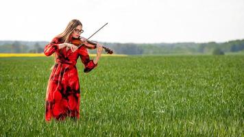 ung kvinna i röd klänning som spelar fiol i grön äng - bild foto