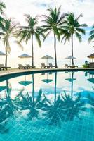 vackra lyxparaplyer och stolar runt en utomhuspool på hotell och resort med kokospalmer vid solnedgång eller soluppgång - semester- och semesterkoncept foto