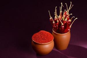 kyligt pulver med röd kyligt i lerkrukor, torkade chili på mörk bakgrund foto