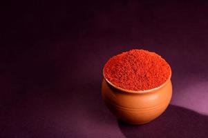 röd chilipeppar pulver i lerkruka på mörk bakgrund foto
