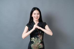 glad vacker ung asiatisk kvinna bär kinesisk traditionell klänning på grå bakgrund foto