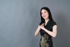 glad vacker ung asiatisk kvinna bär kinesisk traditionell klänning på grå bakgrund foto