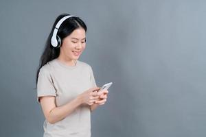 asiatisk kvinna bär trådlös hörlurar hålla smartphone tittar på telefonens skärm med mobilspelare app lyssnar online musik, lär sig främmande språk, tittar på video avkopplande på grå bakgrund foto