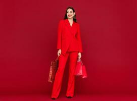 attraktiv kvinna i röd med handla påsar försäljning på röd bakgrund foto