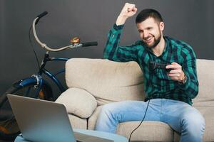 ung hipster stilig skäggig man Sammanträde på soffa på Hem, spelar video spel foto