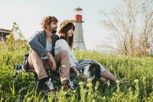 Sammanträde i gräs ung eleganta hipster par i kärlek gående med hund i landsbygden foto
