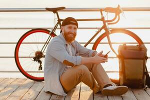 stilig skäggig man reser med cykel i morgon- soluppgång förbi de hav foto