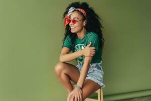 attraktiv svart afrikansk amerikan kvinna Framställ i eleganta hipster utrusta på grön bakgrund foto
