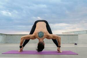 attraktiv hansome man med atletisk stark kropp håller på med morgon- yoga asana utomhus foto