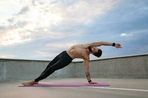 attraktiv hansome man med atletisk stark kropp håller på med morgon- yoga asana utomhus foto