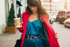 eleganta kvinna i röd täcka gående i gata med kaffe foto