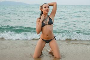 ung skön blond kvinna solbad på sand strand i bikini simning kostym, årgång halsband foto