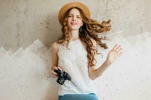 ung Söt leende Lycklig kvinna i sugrör hatt innehav årgång Foto kamera, lång lockigt hår