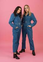 två upphetsad attraktiv flicka vänner aktiva kvinnor Framställ på rosa bakgrund i denim övergripande har roligt tillsammans mode trend foto