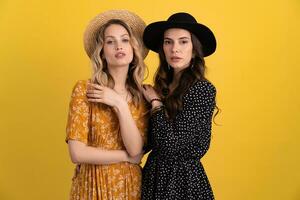 skön kvinnor vänner tillsammans isolerat på gul bakgrund i svart och gul klänning och hatt foto