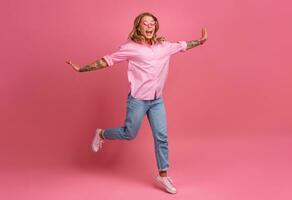 blond Söt kvinna i rosa skjorta och jeans leende Hoppar foto